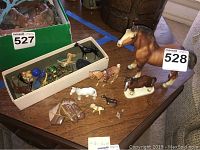 View of collection showing various vintage animal figures including horses in different sizes and materials, laid out on a wooden table with one boxed set included.
