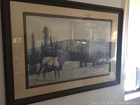 Framed wilderness elk deer print hung on wall showing elk standing in forested landscape.