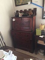 Full view of closed Norwegian carved secretary desk with carved details, drawers, and items on top.