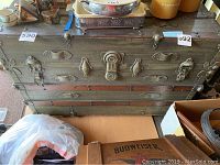Wooden storage trunk with metal locks and hardware, showing wear and damage on surface.