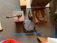 Photo showing cast iron waffle iron with lid, wooden hand crank coffee grinder, and vintage cast iron clothes irons with wooden handles on carpet floor.