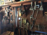 Wall-mounted workshop tools including saws, scrapers, scissors, pliers, clamps, and hardware.