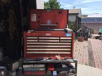 Red steel toolbox with hinged lid open, sitting on a metal rolling cart outdoors