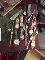 Overview of 12 wrist watches laid out on wooden surface