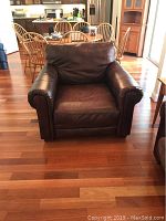 Front view of one brown leather-look armchair showing rolled arms and cushioned back and seat in a wood-floored room.