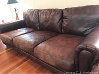 Front view of three-seat brown faux leather sofa on hardwood floor