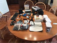 Tabletop overview showing various electronics and accessories including keyboards, cameras, containers of batteries, cables.