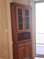 Front and angled view of wooden corner cabinet with glass windowed doors on top, open shelf, drawer, and closed bottom cabinet.