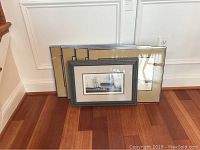 Five framed artworks resting against wall on hardwood floor, varying sizes about 19x14 to 21x19 inches