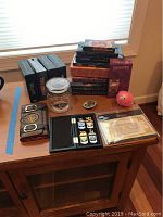 Overall view of Harry Potter book stack, DVD box sets, wallet, Honeydukes candy jar, collectible medal badges in black box, and some other small items on wooden table near window.