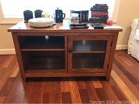 Front view of the wooden cabinet showing the open shelf on the left and glass door on the right with items placed on top.