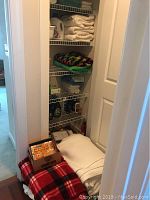 Closet with shelves holding folded white towels, multi-colored crocheted blanket, various cleaning products such as spray bottles and liquid detergents.