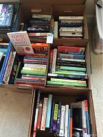 Top view of multiple stacked boxes of books including fiction and reference categories.