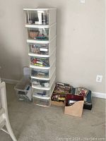 Full view of eight stacked clear plastic storage bins and additional baskets on floor containing various office, craft, and storage supplies.