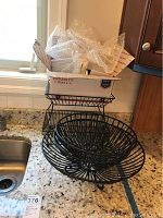 Three circular black metal baskets stacked with a two-tiered black metal basket and a box of hardware on top on a kitchen counter