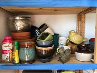 Shelf holding various ceramic and metal planters, garden figurines, and plant food bottles