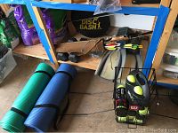 Wide shot of the assortment of sporting goods including yoga mats, bow and arrows, tennis balls, hand weights, flippers, and Disc Bash game.