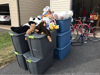 Overall view of multiple large plastic bins filled with assorted stuffed animals and plush toys placed outside a garage.