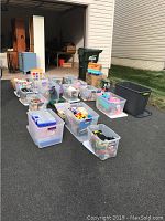 Photo showing multiple clear plastic storage bins arranged outside, filled with various toys and games.