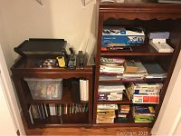 Two wooden shelving units filled with office supplies including binders, papers, file folders, and the boxed ComboBind C50 binding system on top shelf with envelopes and papers beneath.