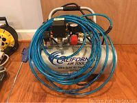 Full view of California Air Tools Ultra Quiet Air Compressor model 2010A with coiled blue air hose in front.