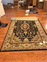 Full view of the rectangular area rug laid on hardwood floor showing black central medallion design with floral elements and beige border.
