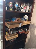 Photo of wooden storage shelves with various modeling supplies such as spray paint cans, paint jars, glues, and other containers organized on pull-out trays.