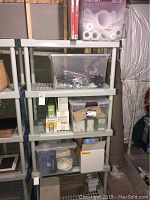 Shelving unit with several plastic storage containers holding locks, chains, respirators, lighting components, and miscellaneous items