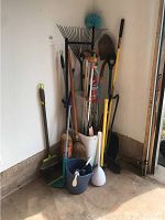 Wide view of rack with yard and cleaning tools arranged in corner including rakes, shovels, brooms, buckets and crutches