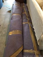 Three large area rugs rolled and secured with tape, stacked side by side in a storage or garage space.