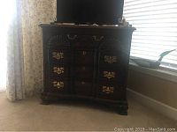 Front view of a dark wood chest of drawers by Harden with brass handles and carved shell design details