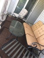 View of two metal outdoor chairs with beige cushions and black metal outdoor table with glass top on porch