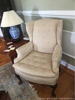 Wingback chair shown front angled view with side arms and tufted seat cushion on wooden legs.
