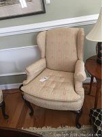 Front view of the upholstered wingback chair showing shape, fabric pattern, and wooden legs.