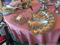 Photo of vintage silver-toned deviled egg tray, glass serving plate, and other silver serving pieces on pink tablecloth.