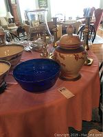 Blue glass bowl, ginger jar, and hurricane shade displayed on table with other items and surroundings visible in background.