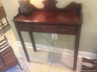 Full view of the wood console table showing its carved top and single drawer with brass pulls.