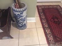 Full view of the blue and white ceramic umbrella stand placed on tiled floor, showing its tall cylindrical shape and artistic design.