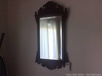 Full view of the carved wood framed mirror showing its dark wood and beveled glass.