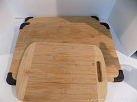 Three wooden cutting boards stacked: two large with rubber corners and one smaller without rubber corners