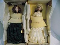 Both dolls in their boxes with foam padding showing their full outfits and partial faces.