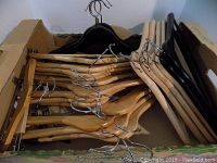 Box filled with wooden hangers, some with clips attached for pants or skirts, some regular wooden hangers