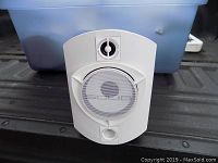 Front view of white wall mount Rocksolid Sounds speaker showing woofer behind metal grille, tweeter above, and bass port below.