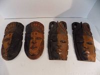 Four wooden hand-carved masks arranged side by side showing front view of masks.