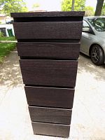 Front view of dark brown tall narrow wood chest showing six drawers.