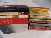 Books stacked showing titles and authors. Mix of hardcover and paperbacks, diverse fiction collection.