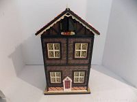 Front view of the closed musical Christmas house, showing its 16-inch tall brick and wood design with windows and red door.