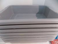 Stack of 7 gray Rubbermaid commercial bus bins stacked horizontally showing sides and rims.