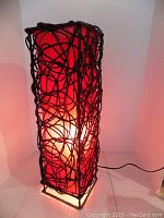 Side view of the wicker lamp illuminated showing the woven wicker exterior and red fabric interior glowing warmly