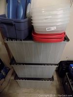 Stack of 3 large translucent clear bins with black lids and 7 smaller clear bins stacked on top with red lids beneath.